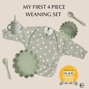 Puede incluir: Un juego de cuatro piezas para el destete del bebé en verde con un babero con estampado de corazones, dos cuencos y una cuchara. El juego es adecuado para bebés de 6 meses en adelante. El embalaje incluye el texto "My First 4 Piece Weaning Set" y "Made for Mums Awards 2024 Silver".