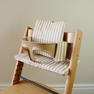 May include: A wooden high chair with a tan plastic tray and striped cushions. The cushions and backrest are beige with vertical brown stripes. The chair has a black footrest and is designed for a baby or toddler.