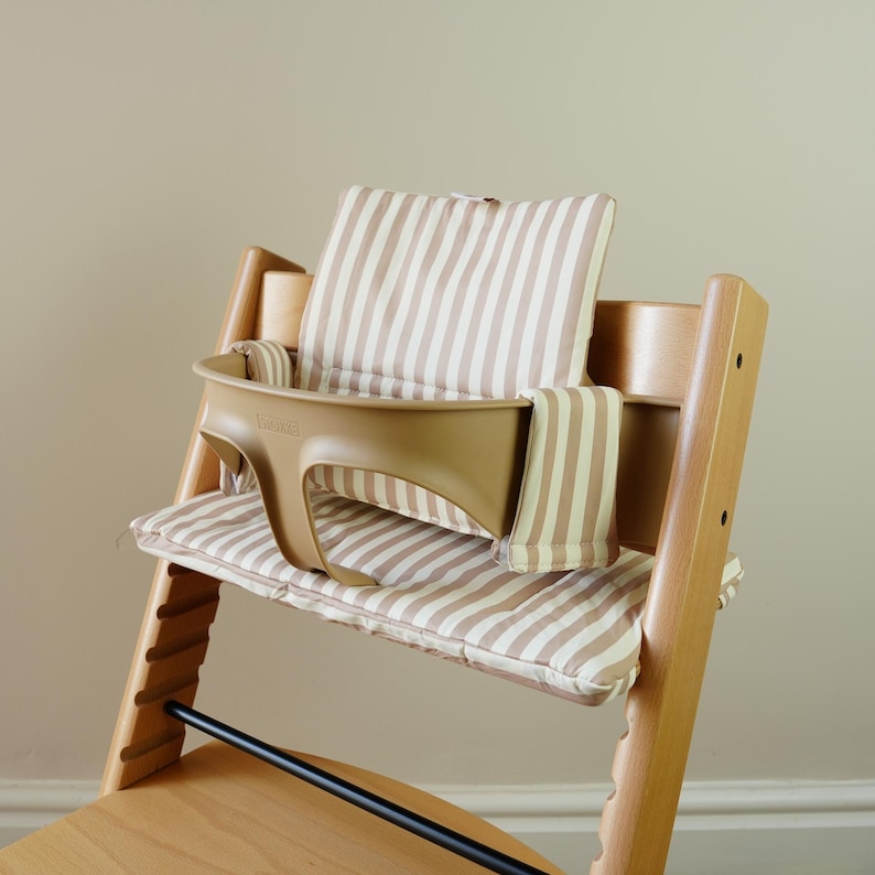 May include: A wooden high chair with a tan plastic tray and striped cushions. The cushions and backrest are beige with vertical brown stripes. The chair has a black footrest and is designed for a baby or toddler.