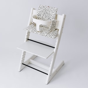 May include: White high chair with a black and white polka dot seat cushion. The chair has a tray and a safety harness.