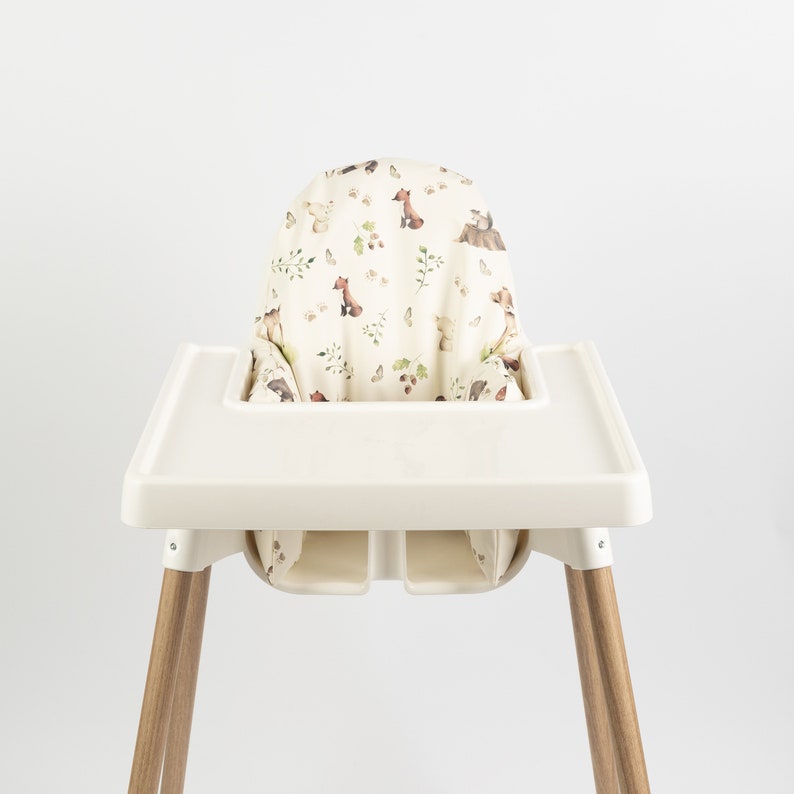 Puede incluir: Una trona con asiento y bandeja color crema, y patas de madera. La funda del asiento presenta un estampado de criaturas del bosque como zorros y osos, junto con hojas y mariposas, sobre un fondo crema. Para beb&eacute;s y ni&ntilde;os peque&ntilde;os.