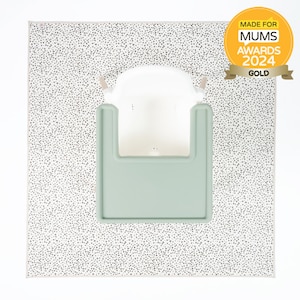 Op de afbeelding: Een witte hoge stoel met een groene lade staat op een witte en zwarte stippen speelmat. De mat heeft een "Made for Mums Awards 2024 Gold" sticker in de rechterbovenhoek.
