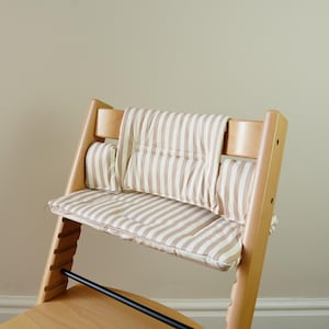 May include: A wooden high chair with a striped cushion and backrest. The cushion and backrest feature a beige and white striped pattern. The chair has a natural wood finish and a black metal footrest.