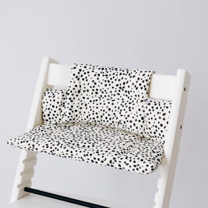 May include: White high chair with a black and white spotted cushion. The cushion has a separate back and seat cushion.