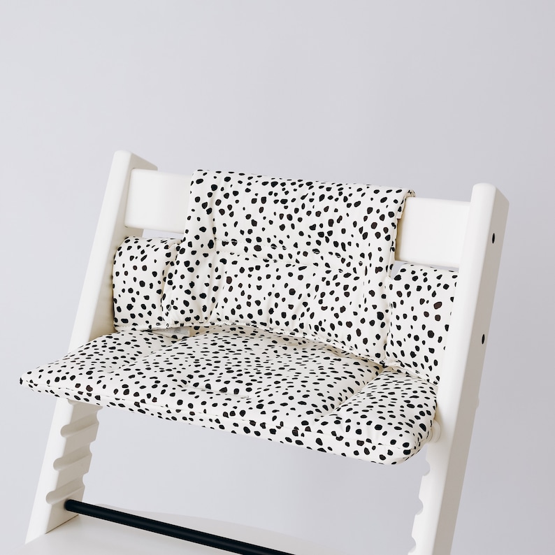 May include: White high chair with a black and white spotted cushion. The cushion has a separate back and seat cushion.