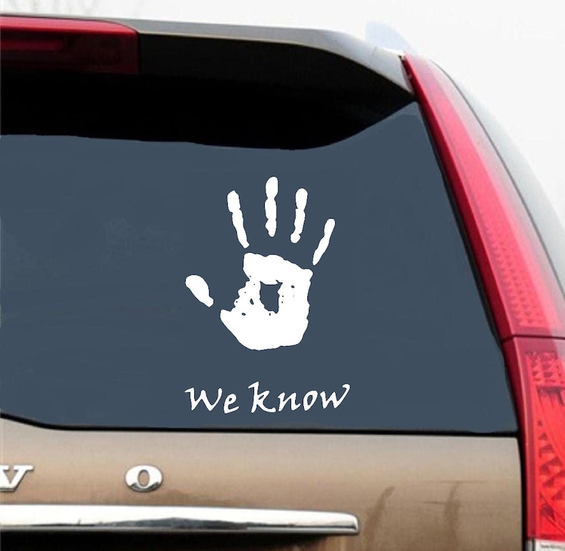 Peut inclure: Un autocollant de main blanche avec le texte "We know" sur une voiture brune. L'autocollant est sur la vitre arri&egrave;re de la voiture.