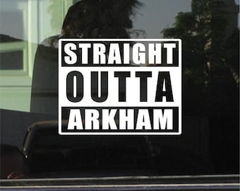 May include: A white and black sticker with the text "STRAIGHT OUTTA ARKHAM" in a bold, blocky font. The sticker is rectangular and has a black border. The sticker is on a window.