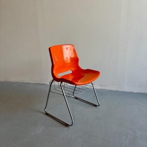 Può includere: Una sedia in plastica arancione con struttura in metallo cromato. La sedia ha schienale e seduta curvi e una griglia metallica sotto la seduta. La sedia è un design moderno della metà del secolo.