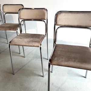 Può includere: Set di quattro sedie vintage con struttura cromata e rivestimento in velluto color talpa. Le sedie hanno un design semplice ed elegante, con schienale e seduta rettangolari. Le gambe sono sottili e leggermente affusolate.
