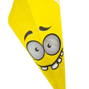 Könnte beinhalten: Ein gelber Papierkegel mit einem darauf gedruckten Comic-Gesicht. Das Gesicht hat große Augen, ein breites Lächeln und eine einzige hochgezogene Augenbraue.