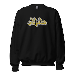 Puede incluir: Sudadera negra con un gráfico "Alpha" amarillo y negro.