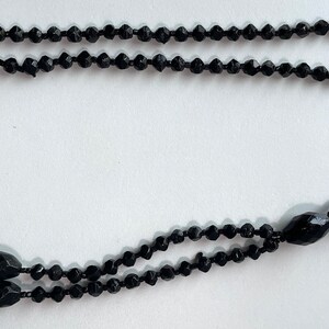 K&ouml;nnte beinhalten: Eine schwarze Perlenkette mit Quaste. Die Kette besteht aus kleinen, facettierten Perlen und hat eine lange, herabh&auml;ngende Quaste am Ende.