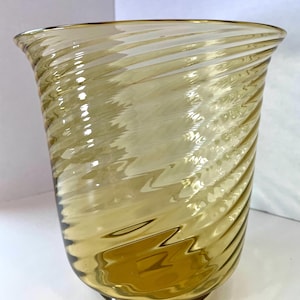 May include: A clear, amber-colored glass vase with a spiral design. The vase has a wide mouth and a slightly flared shape. The glass has a textured appearance, with the spiral pattern creating a visual effect. The vase is suitable for decorative purposes.