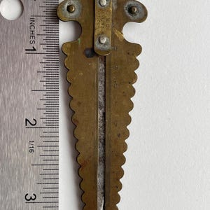 May include: A brass measuring tool with a fleur-de-lis design at the top. The tool has a scale marked in inches and a small, pointed blade. The text "D.M.GOO. & CO. PAT. SEP. 23, 1897.  BPT. COA." is engraved on the tool.