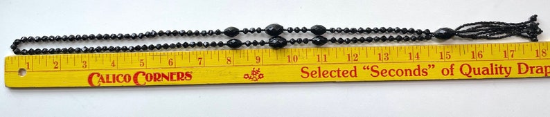 K&ouml;nnte beinhalten: Eine schwarze Perlenkette mit Quaste, gemessen auf einem Lineal mit einer L&auml;nge von 18 Zoll. Das Lineal tr&auml;gt den Text "Calico Corners" und "Selected "Seconds" of Quality Drapery".