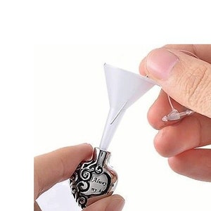 Puede incluir: Un relicario de cremación en forma de corazón de plata con la inscripción "Siempre en mi corazón". Se utiliza un pequeño embudo de plástico para llenar el recipiente.