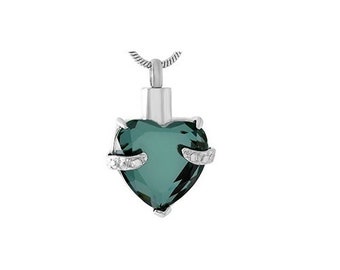 May include: A silver heart-shaped cremation pendant with a dark green crystal and small clear stones on the sides. The pendant is on a silver chain.