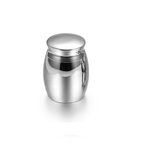 Può includere: Un'urna in metallo argentato con un coperchio incernierato e un manico ad anello. L'urna è progettata per contenere ceneri.