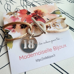 Peut inclure: Un bracelet en argent avec un charme qui dit "18". Le bracelet est fait d'un cordon doré et a un fermoir à glissière en argent. Le bracelet est sur une carte blanche avec le texte "Un cadeau pour toi... Mademoiselle Bijoux https://mllebijoux.fr"