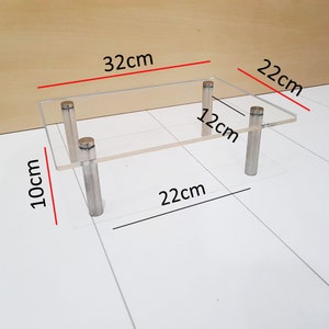 May include: A clear acrylic shelf with four silver metal legs. The shelf measures 32 cm by 22 cm and is 12 cm high. The shelf is 10 cm tall.