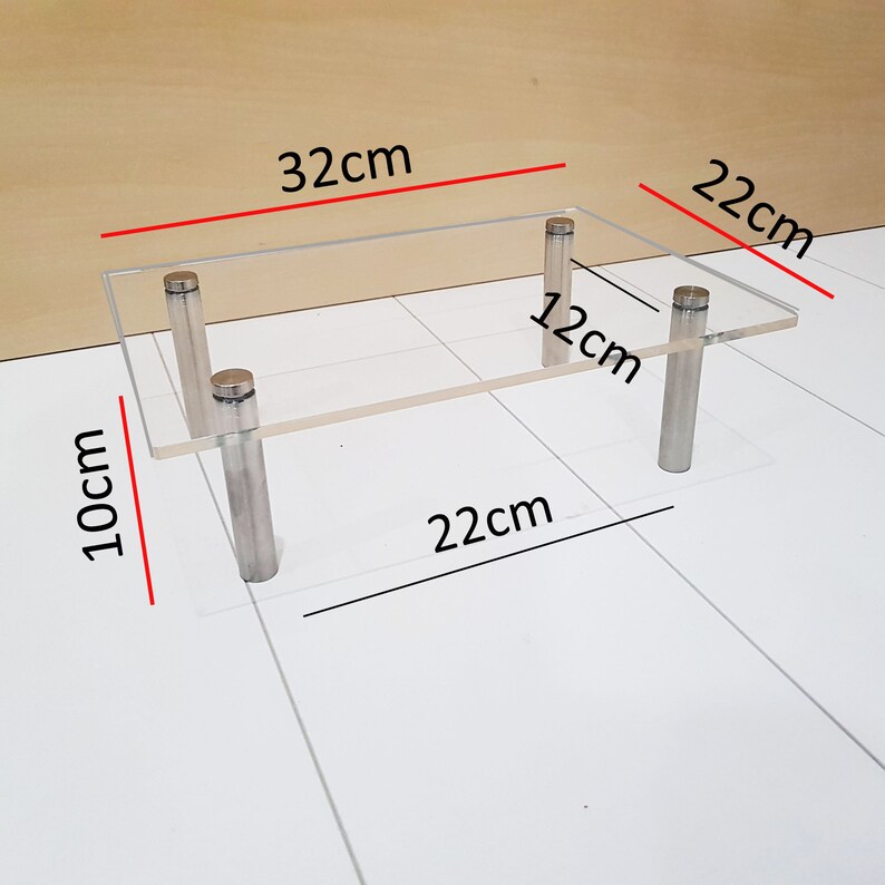 May include: A clear acrylic shelf with four silver metal legs. The shelf measures 32 cm by 22 cm and is 12 cm high. The shelf is 10 cm tall.