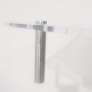 May include: A clear acrylic shelf with a silver metal bracket. The shelf is mounted to a white wall.
