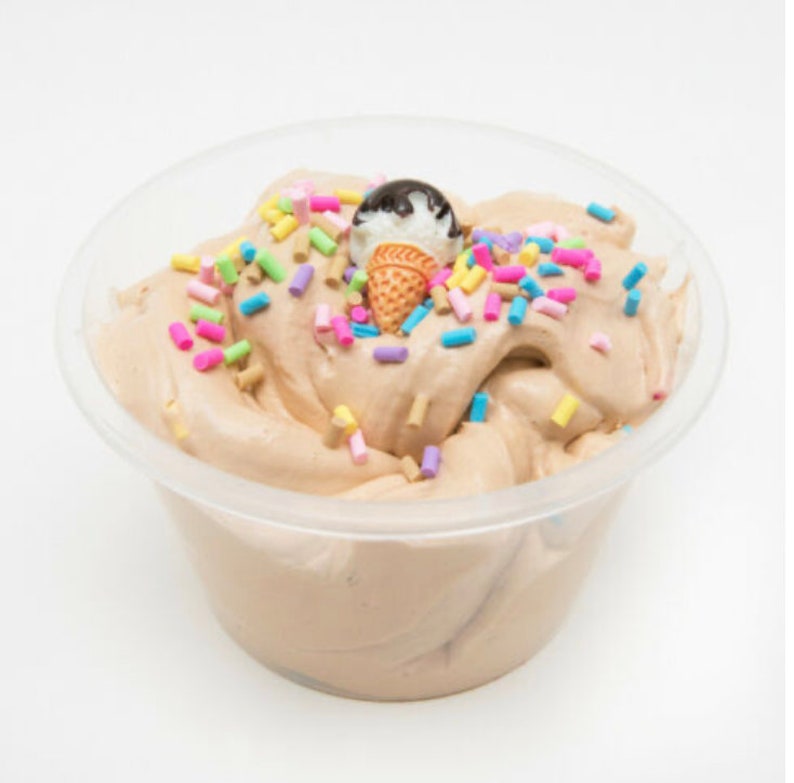 Puede incluir: Un recipiente de pl&aacute;stico transparente lleno de slime marr&oacute;n chocolate cubierto con chispas de colores y un peque&ntilde;o cono de helado de chocolate.