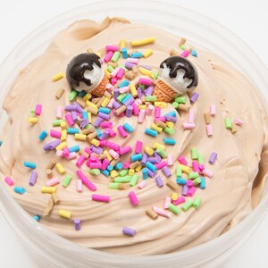 Puede incluir: Primer plano de una slime marr&oacute;n con chispas de colores y dos conos de helado de chocolate en miniatura en la parte superior.