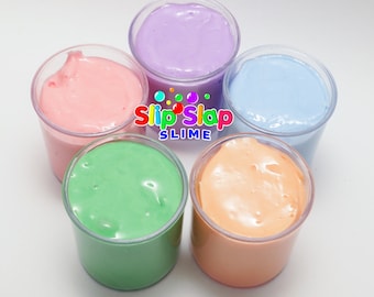 Puede incluir: Cinco vasos transparentes llenos de slime de diferentes colores. Los colores del slime son rosa claro, verde claro, naranja claro, azul claro y morado claro. Los vasos están dispuestos en círculo sobre una superficie blanca. El texto "Slip 'n' Slap Slime" está impreso en el centro de la imagen.
