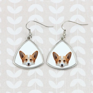 May include: A pair of silver triangle-shaped earrings with a white background and a geometric image of a corgi dog's face.