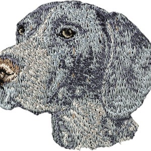 Könnte beinhalten: Gestickter Aufnäher mit dem Kopf eines grau-weißen Hundes im Profil. Der Hund hat einen ernsten Ausdruck und seine Ohren sind schlaff.