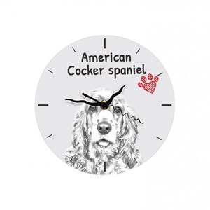 May include: Round wall clock featuring a sketch of an American Cocker Spaniel. The clock face is light gray with black hands and the words "American Cocker Spaniel" in black. A red paw print with a heart is also on the clock face.