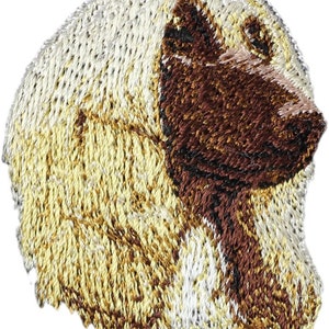 May include: Embroidered patch of a white and brown Afghan Hound dog's head. The dog's fur is detailed with white, brown, and gold thread.