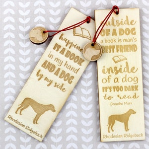 May include: Two wooden bookmarks with a Rhodesian Ridgeback dog silhouette and a quote about dogs and books. The first bookmark reads "Happiness is a book in my hand and a dog by my side". The second bookmark reads "Outside of a dog, a book is man's best friend. Inside of a dog, it's too dark to read. - Groucho Marx".