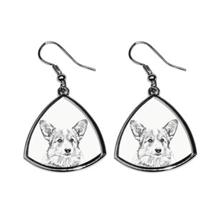May include: A pair of silver dangle earrings with a white triangle-shaped pendant featuring a black and white illustration of a corgi dog.