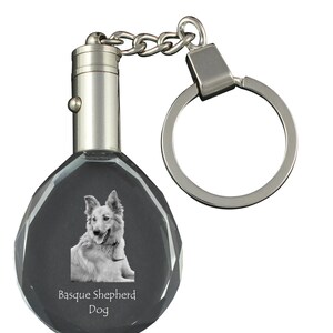 Peut inclure: Un porte-clés argenté avec un charme en cristal représentant une photo en noir et blanc d'un chien de berger basque. Le charme est gravé des mots "Basque Shepherd Dog".