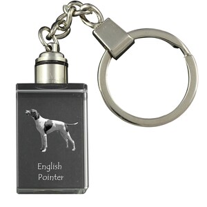 Puede incluir: Un llavero plateado con un dije de cristal negro que presenta un perro Braco Inglés blanco y negro con el texto "English Pointer" en el dije.