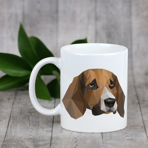 May include: White ceramic mug with a geometric illustration of a brown and white dog's head. The dog has brown eyes and a black nose.