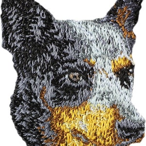 May include: Embroidered patch of a blue heeler dog's head with black, brown, and white fur. The dog is looking to the right.