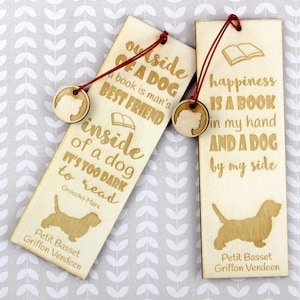 May include: Two wooden bookmarks with a dog silhouette and text. The first bookmark says "outside of a dog a book is man's best friend inside of a dog it's too dark to read Groucho Marx". The second bookmark says "happiness is a book in my hand and a dog by my side". Both bookmarks have a small wooden dog charm attached.
