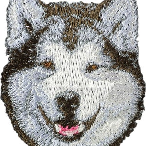Könnte beinhalten: Gestickter Aufnäher mit dem Gesicht eines Wolfes mit braunem Fell, weißen Markierungen und einer rosa Zunge. Der Wolf lächelt.