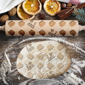 Op de afbeelding: Een houten deegroller met een patroon van harten en de tekst "Ik hou van Engelse muffins" erop. De deegroller ligt op een houten oppervlak met verspreide bloem.