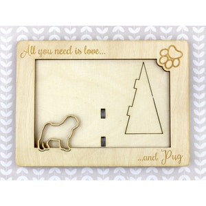 May include: A wooden photo frame with the text "All you need is love... and Pug" engraved on it. The frame has a cutout of a pug dog and a paw print.