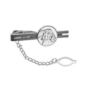 May include: A silver tie clip with a round, white enamel charm featuring a black and white photo of a dog's head. The tie clip has a chain attached to it.
