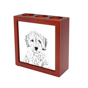 Peut inclure: Un porte-crayons en bois rouge avec trois fentes. Le devant du porte-crayons présente une illustration en noir et blanc d'un chien blanc et moelleux.