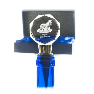 Puede incluir: Un tapón de botella de vidrio transparente con una imagen grabada de un Cocker Spaniel Inglés. El tapón está en una caja de terciopelo azul. El texto "English Cocker Spaniel" está grabado en el tapón.