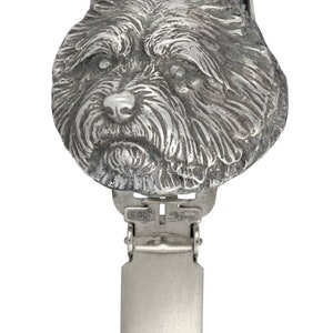 May include: A silver-toned metal dog head charm with a clip on the back. The dog has a fluffy, scruffy coat and is looking straight ahead.