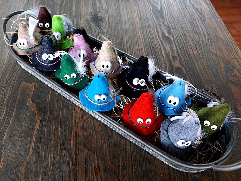 Puede incluir: Una colecci&oacute;n de sombreros de gnomo de fieltro en varios colores, incluyendo rojo, azul, verde, negro y gris. Cada sombrero tiene un pomp&oacute;n blanco y un par de ojos saltones.