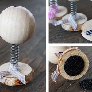 Puede incluir: Una bola de madera en un resorte con una base de madera. La base est&aacute; decorada con una cinta blanca y marr&oacute;n. La bola est&aacute; unida al resorte con un tornillo de metal.