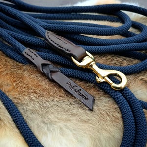 May include: A navy blue dog lead with a braided rope design. The lead has brown leather accents and a gold-coloured metal clasp. The word "Rebalance" is embossed on a leather tag.